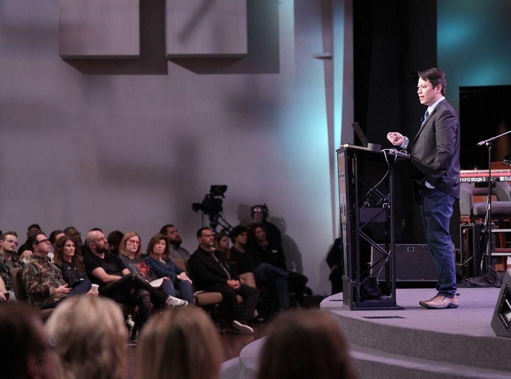 Pastor Steve Cioccolanti teaching at a conference from the podium with keyboard and camera setup